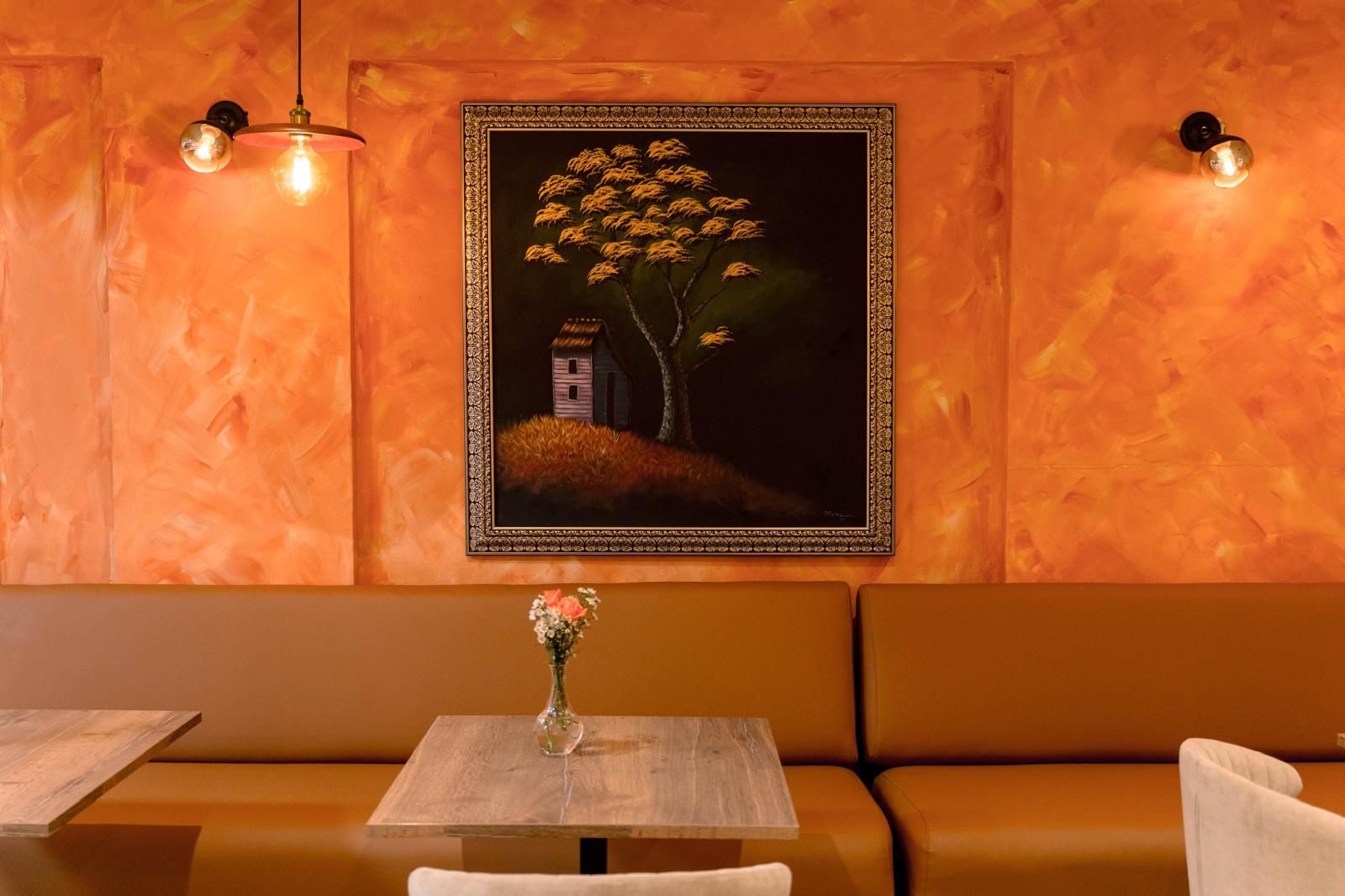 Banqueta y mesa servida junto a una pared naranja con un cuadro enmarcado, en el comedor de La Maison Française