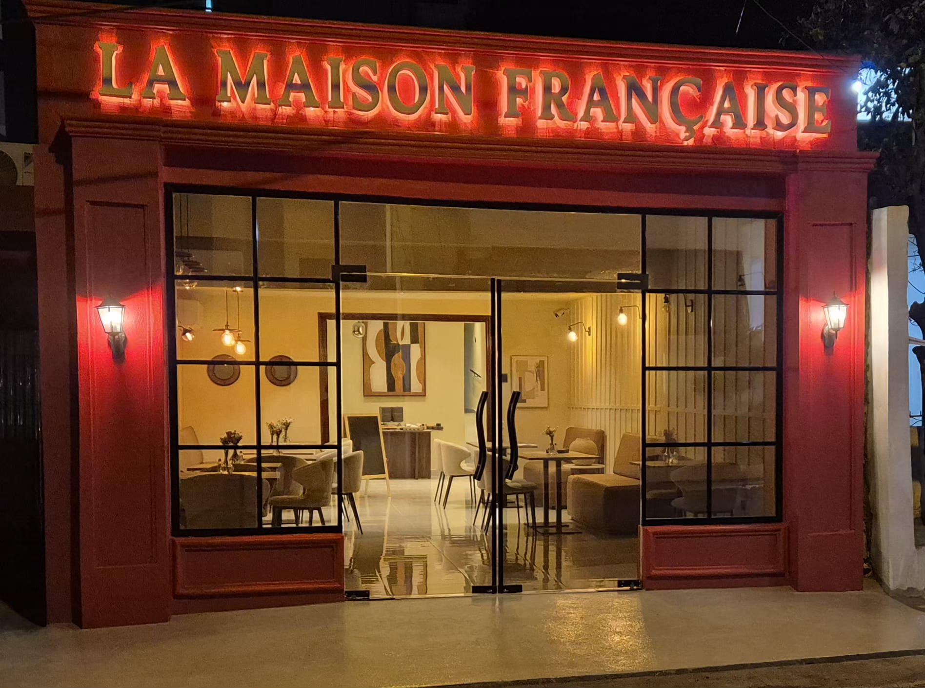 Fachada de La Maison Française de noche, con el rótulo iluminado en la calle Lic. Genaro Pérez, Villa Olga